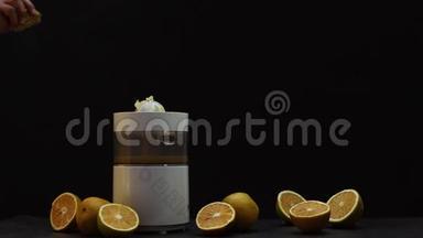 在榨汁机里用手在黑色背景上压榨橙子